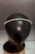 A silver-toned headband adorned with a single row of clear rhinestones, displayed on a black mannequin head bust.