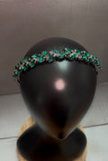 A silver-toned headband embellished with marquise-cut green gemstones and clear rhinestones, displayed on a black mannequin head.