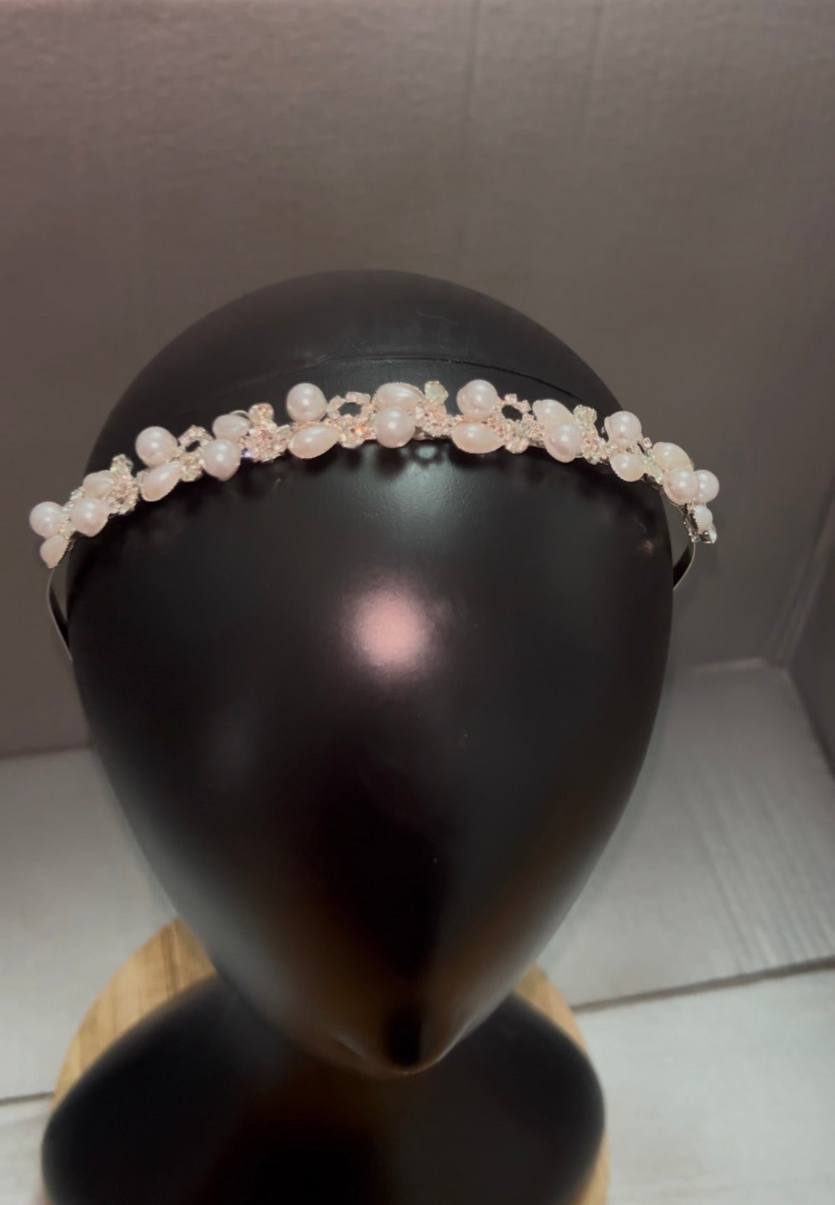 A delicate pearl and crystal headband displayed on a black mannequin head, set against a neutral gray background.