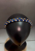 A gold-tone headband embellished with blue and clear rhinestones, displayed on a black mannequin head.