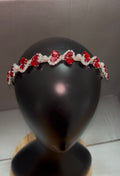 A silver tiara headband decorated with red heart-shaped crystals and white pearls, displayed on a black mannequin head.