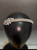 A silver rhinestone headband with a floral cluster on one side and a woven band on the other, displayed on a black mannequin head.
