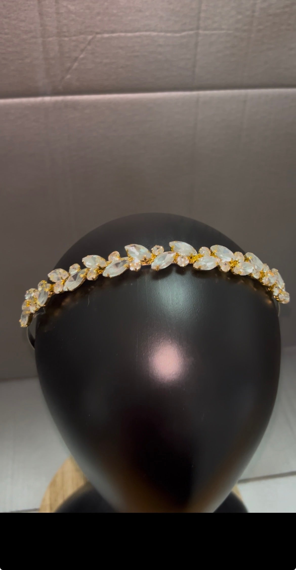 A gold and clear crystal leaf-patterned headband displayed on a black mannequin head against a gray background.
